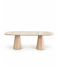 A modern oval dining table with a light beige wood grain top and two sculptural, flared pedestal legs, shown against a solid white background.
