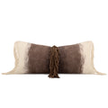 A rectangular throw pillow with a brown and cream cowhide-inspired pattern, featuring cream fringe on the sides and a central brown tassel, shown on a plain white background.