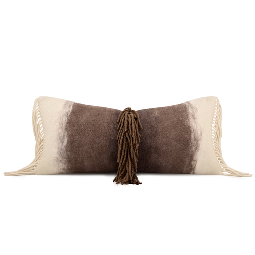 A rectangular throw pillow with a brown and cream cowhide-inspired pattern, featuring cream fringe on the sides and a central brown tassel, shown on a plain white background.